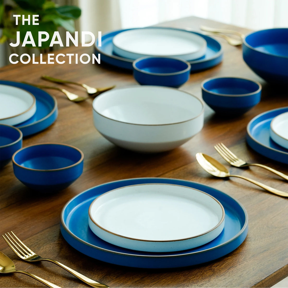 Table setting with blue and white dishes and gold cutlery on a wooden surface, featuring 'The Japandi Collection' text.