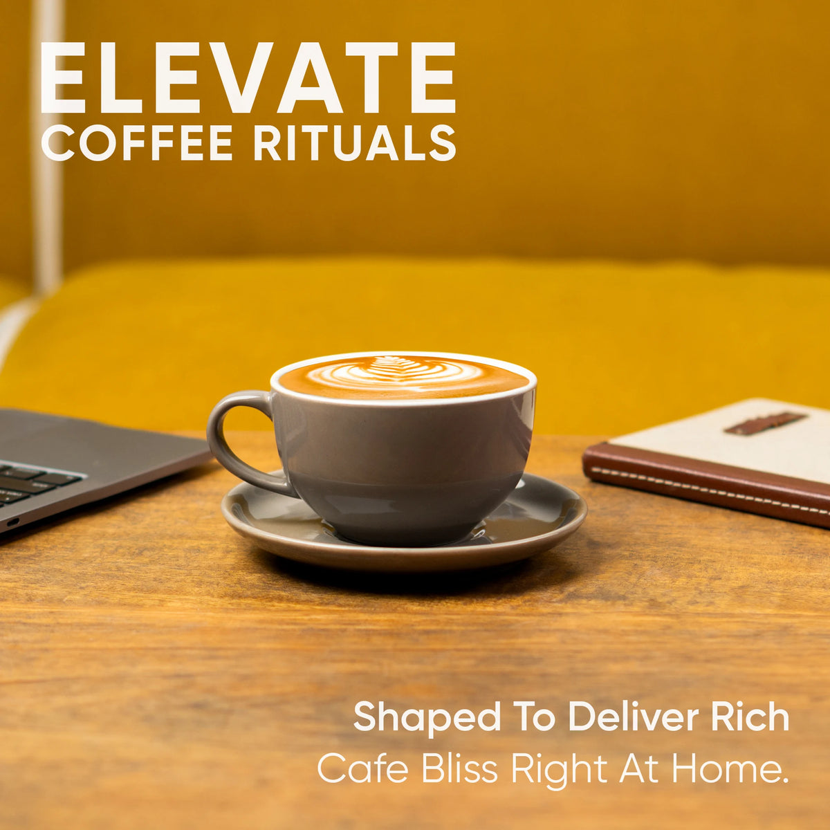 Cup of coffee with latte art on a saucer, laptop, and notebook on a wooden table with 'Elevate Coffee Rituals' text.