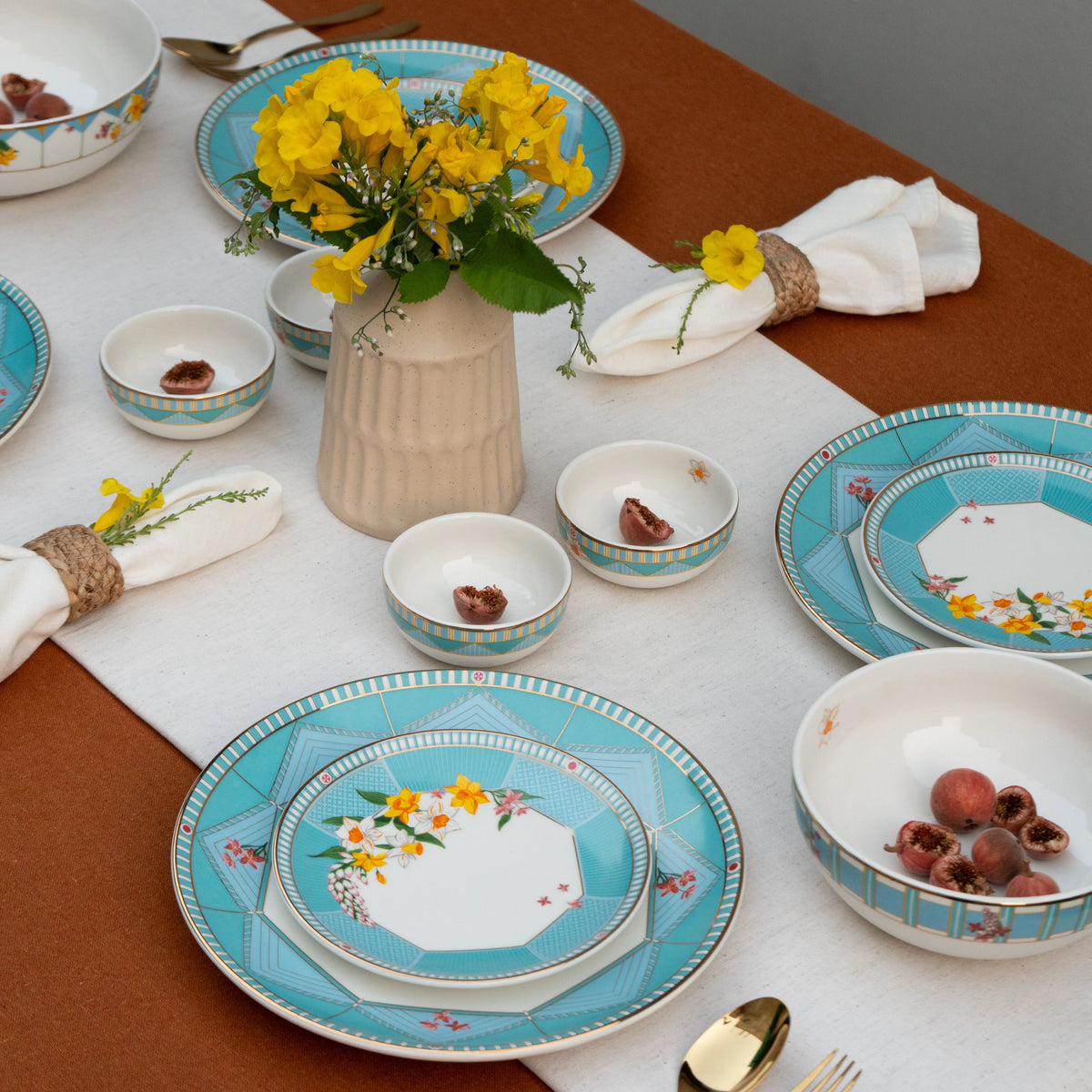 Dining table set with floral-patterned plates, bowls, and a vase of yellow flowers.