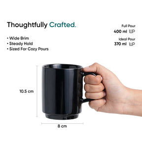 Black mug held by a hand with measurements and text about the mug's features on a white background.