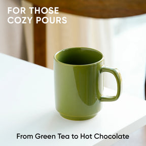 Green mug on a white surface with text about cozy pours and drink options.