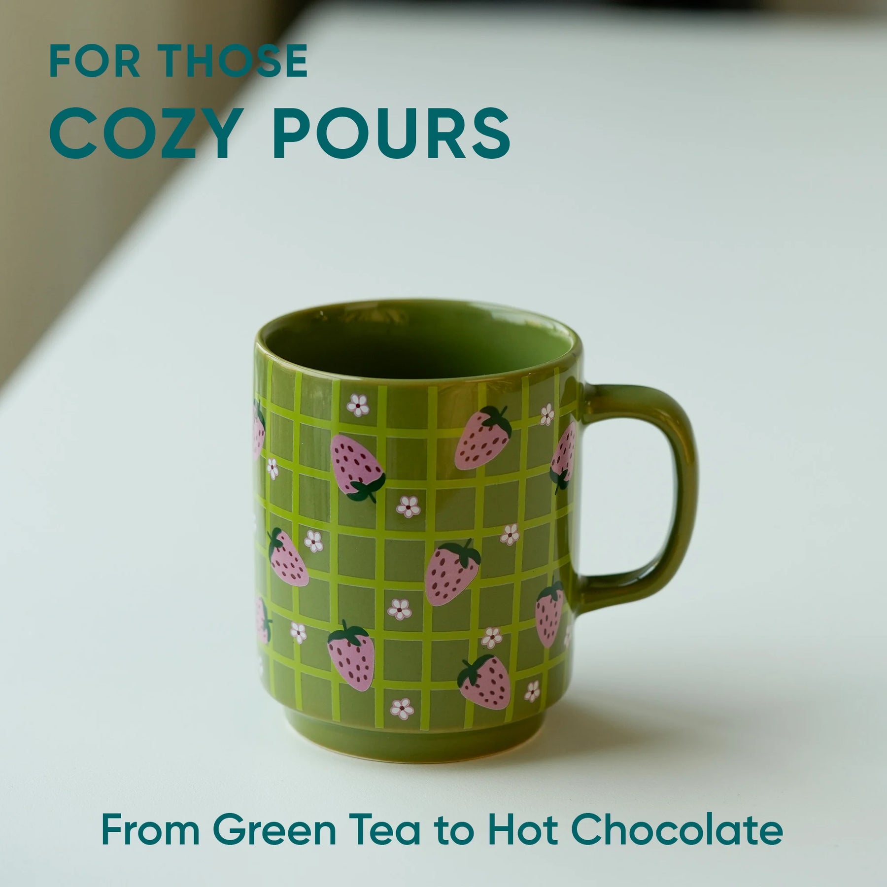 Green mug with strawberry pattern on a white surface, text 'For Those Cozy Pours' and 'From Green Tea to Hot Chocolate'.
