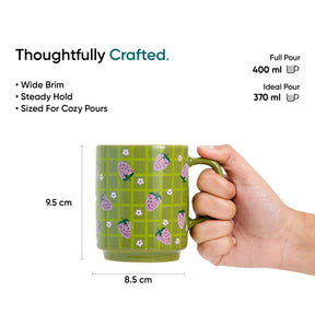 Green mug with strawberry pattern held by a hand, with measurements and text about the mug's features.