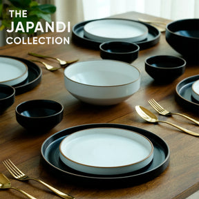 Japandi collection of black and white dishes on a wooden table with gold utensils.
