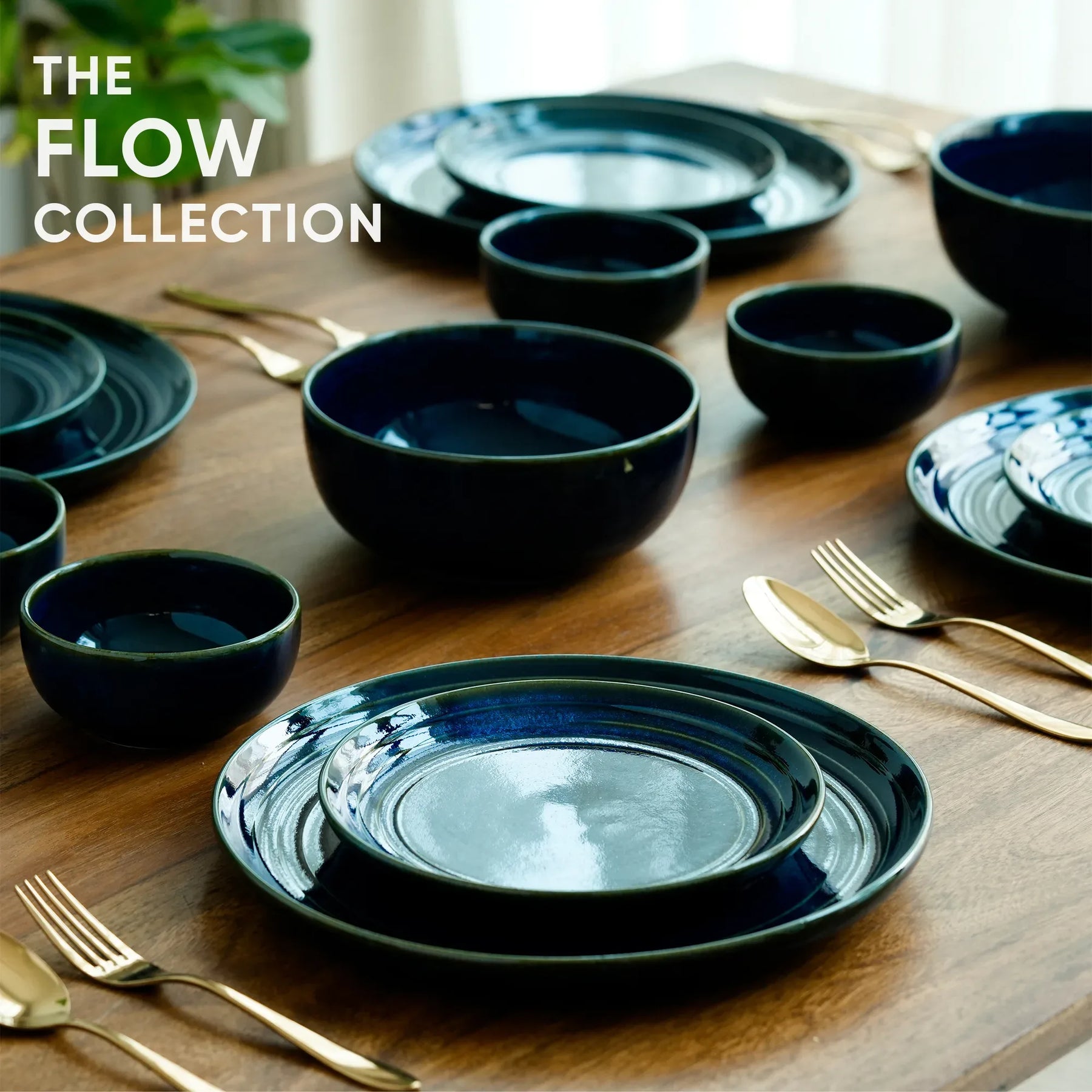 Flow Collection black ceramic plates and bowls on a wooden table with gold utensils.