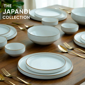 White ceramic dinnerware set with gold rims on a wooden table, labeled 'The Japandi Collection'.