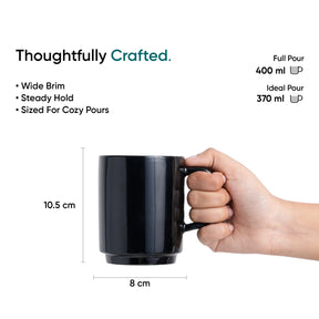 Black mug held by a hand with measurements and text on a white background