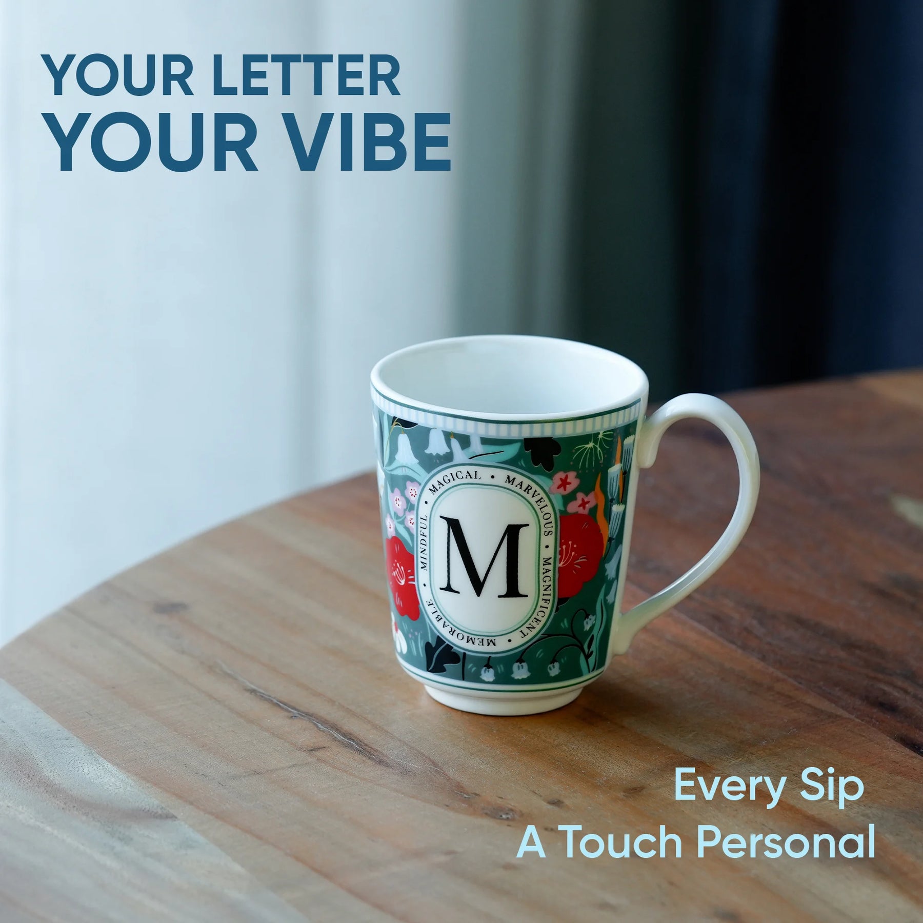 Decorative mug with a letter 'M' on a wooden surface, text 'Your Letter Your Vibe' and 'Every Sip A Touch Personal' displayed.