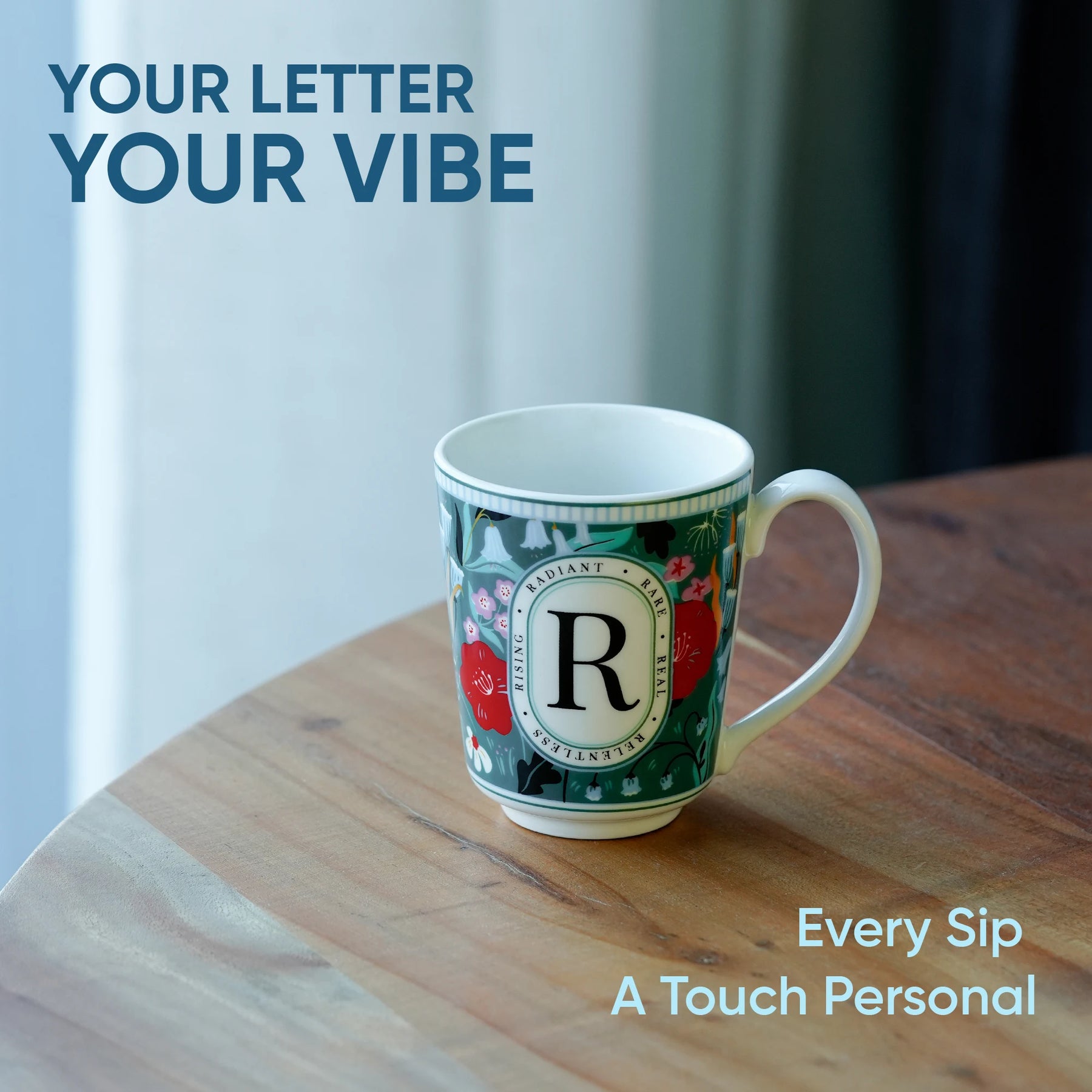 Decorative mug with floral design and letter 'R' on a wooden surface, with text 'Your Letter Your Vibe' and 'Every Sip A Touch Personal'.