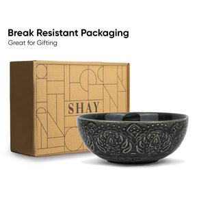 Black ceramic bowl with decorative patterns next to a cardboard box labeled 'SHAY' on a white background.