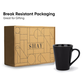 Black mug next to a cardboard box with geometric design and 'SHAY' branding, on a white background.