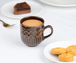 Brown mug with a beverage on a white table with cookies and cake in the background