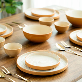 Set of ceramic plates and bowls on a wooden table with cutlery.