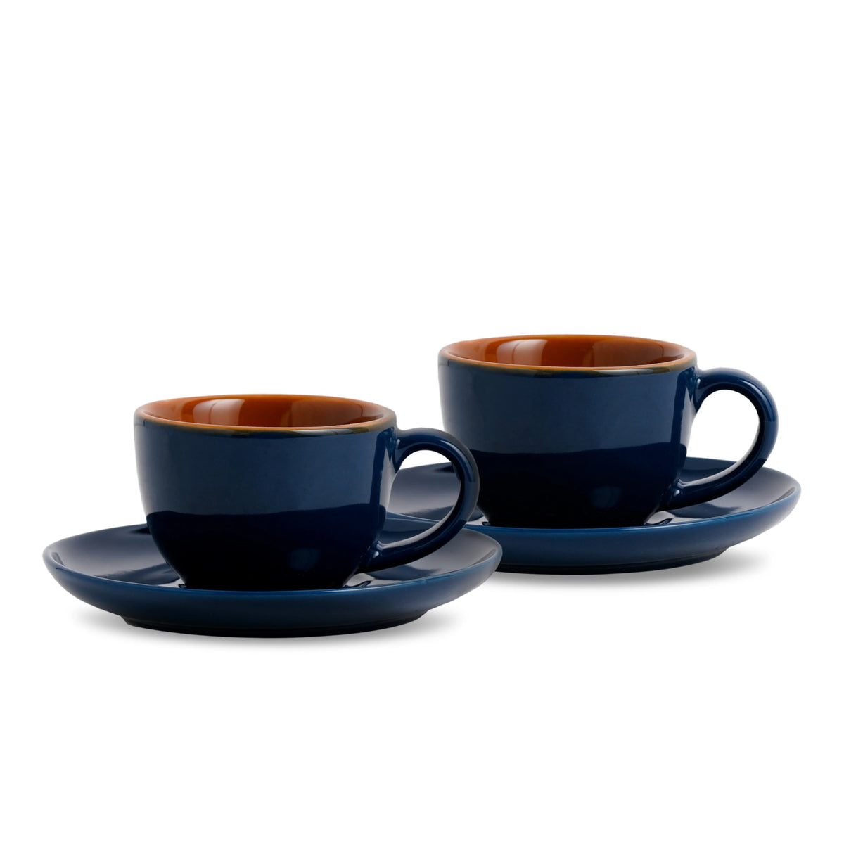 Two navy blue espresso cups with brown interiors on matching saucers against a white background.