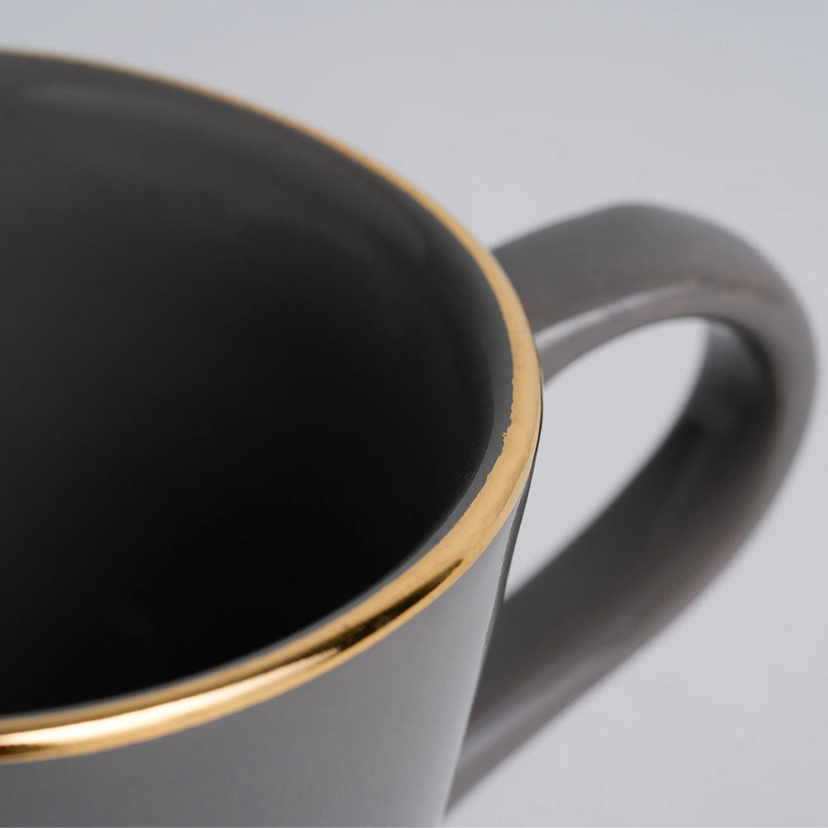 Black mug with gold rim and white handle on a light gray background