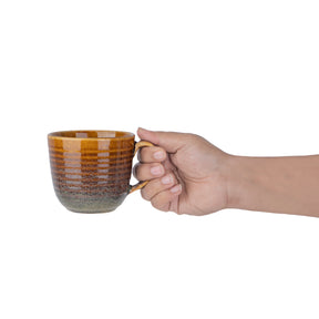 Hand holding a ceramic mug with a gradient design on a white background