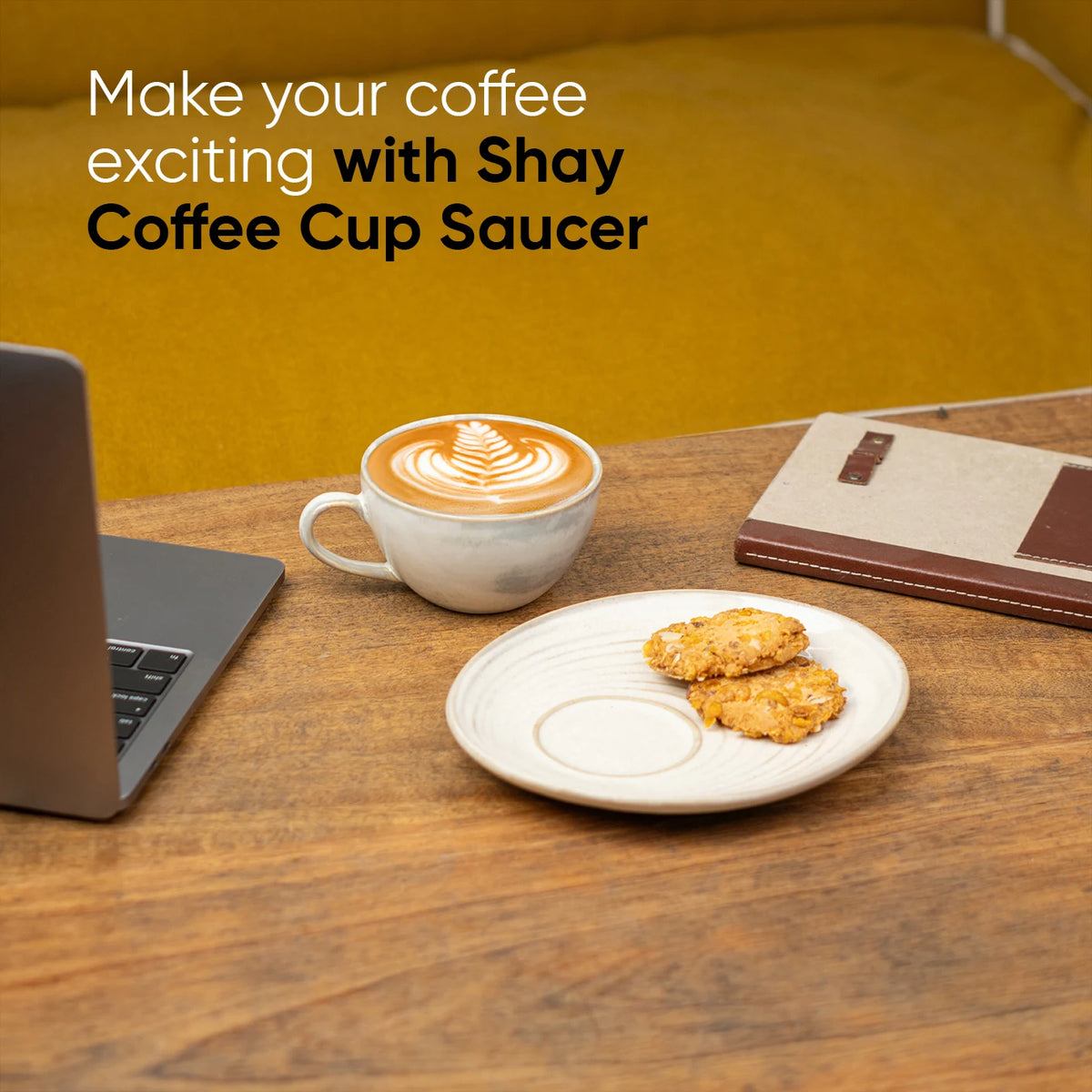 Coffee cup with latte art on a saucer, laptop, and notebook on a wooden table with promotional text for 'Shay Coffee Cup Saucer'.