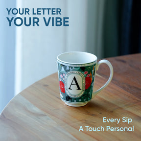 Decorative mug with letter 'A' on a wooden surface, text 'Your Letter Your Vibe' and 'Every Sip A Touch Personal' displayed.