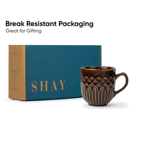 Brown mug with decorative patterns next to a teal and brown box labeled 'SHAY' on a white background.