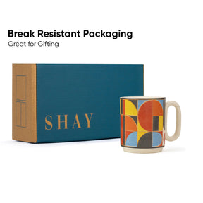 Colorful mug with geometric design next to a 'SHAY' branded box on a white background